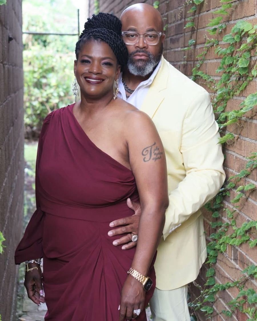 Pop and his wife posing together beside a brick wall with ivy